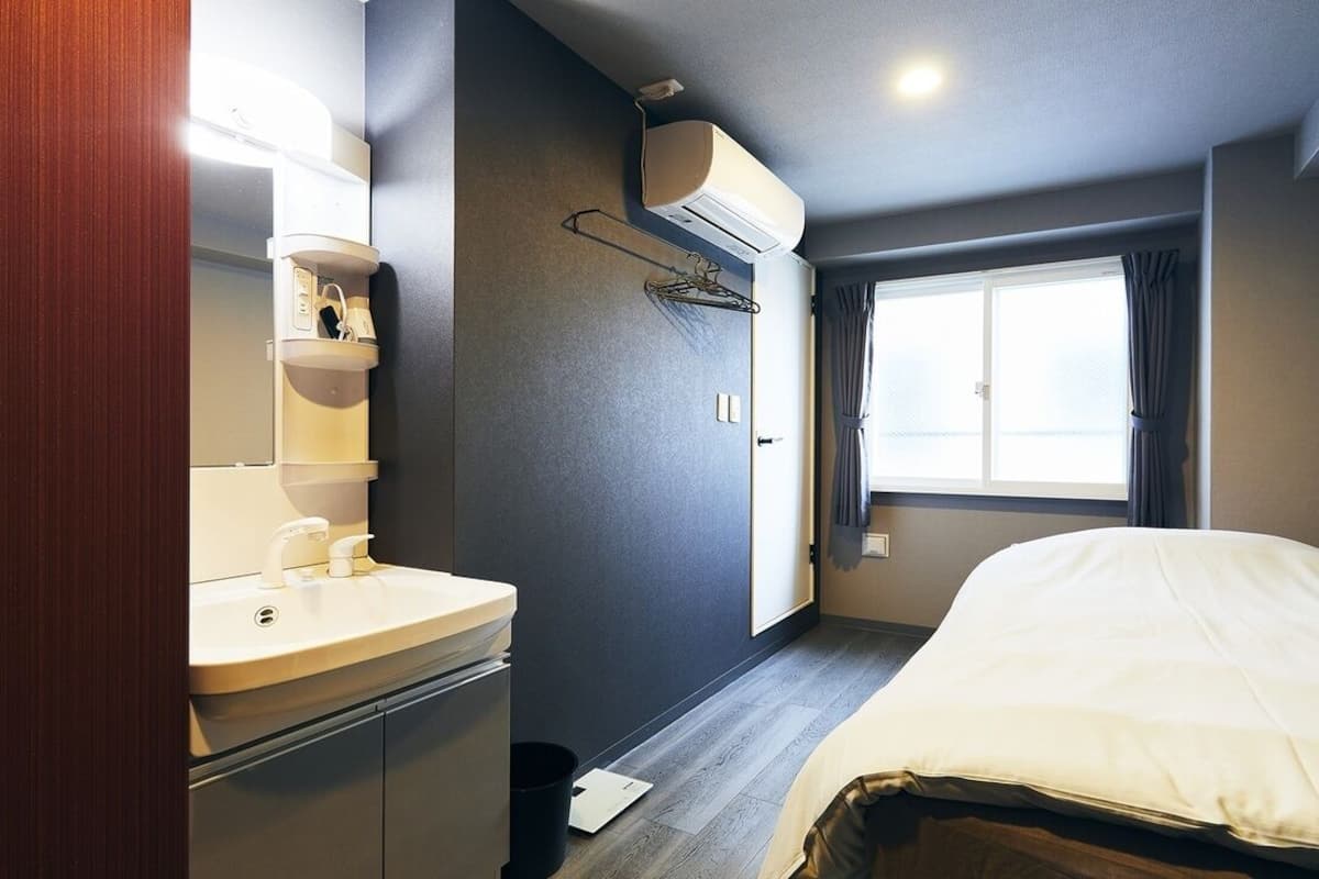 Una habitación de hotel con una cama, una ventana con cortinas, un lavabo y un equipo de aire acondicionado.