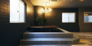 Un intérieur moderne avec des murs recouverts de carreaux foncés, un banc en bois et un lustre.