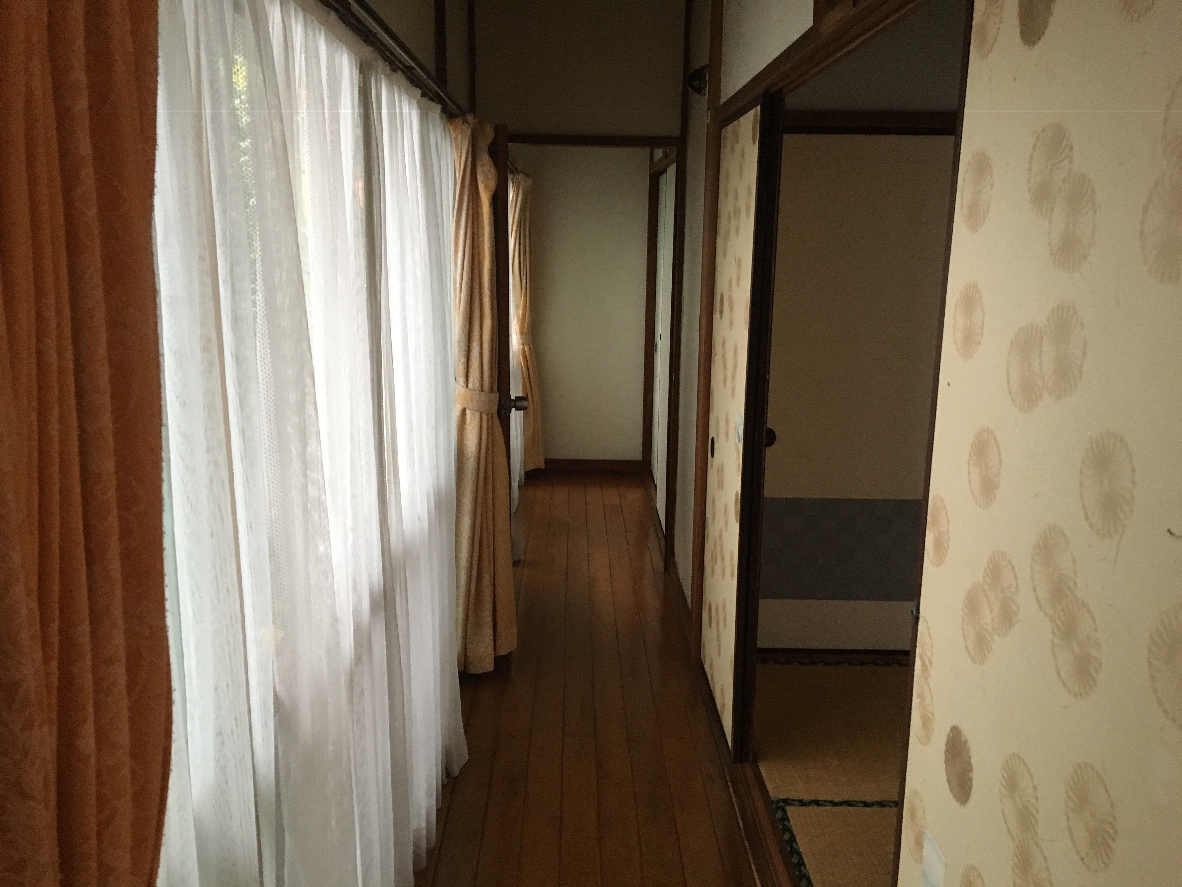 A hallway with wooden flooring, beige walls, and a patterned wallpaper on the right.