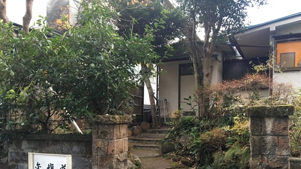 A stone gate with a sign, a narrow stone pathway, and lush greenery. - Kinreisou (Hakone)