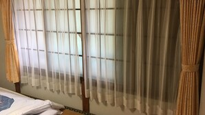 A room with a bed, a window with sheer curtains, and a wooden floor. - Kinreisou (Hakone)