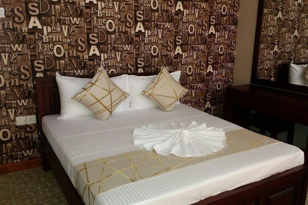 A hotel room with a bed, pillows, a bedside table, a mirror, and a wall with words.
