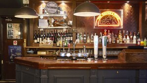Un bar con mostrador de madera, varias botellas de alcohol y un letrero de neón.
