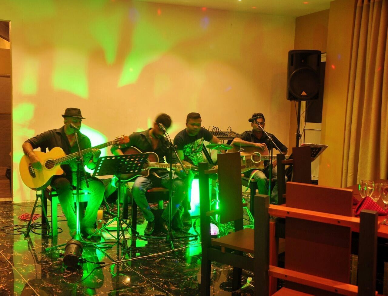 A band performing in a room with a piano, a keyboard, and a drum set.