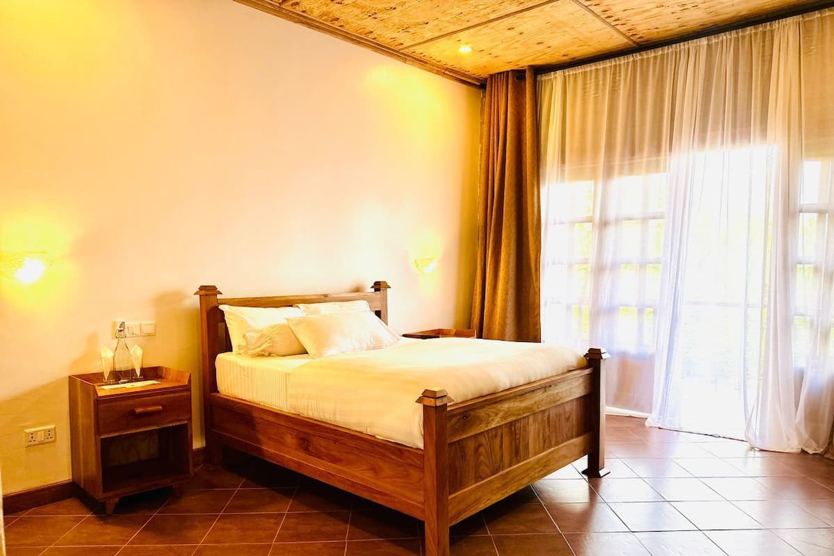 A wooden bed with a nightstand, a window with curtains, and a tiled floor.