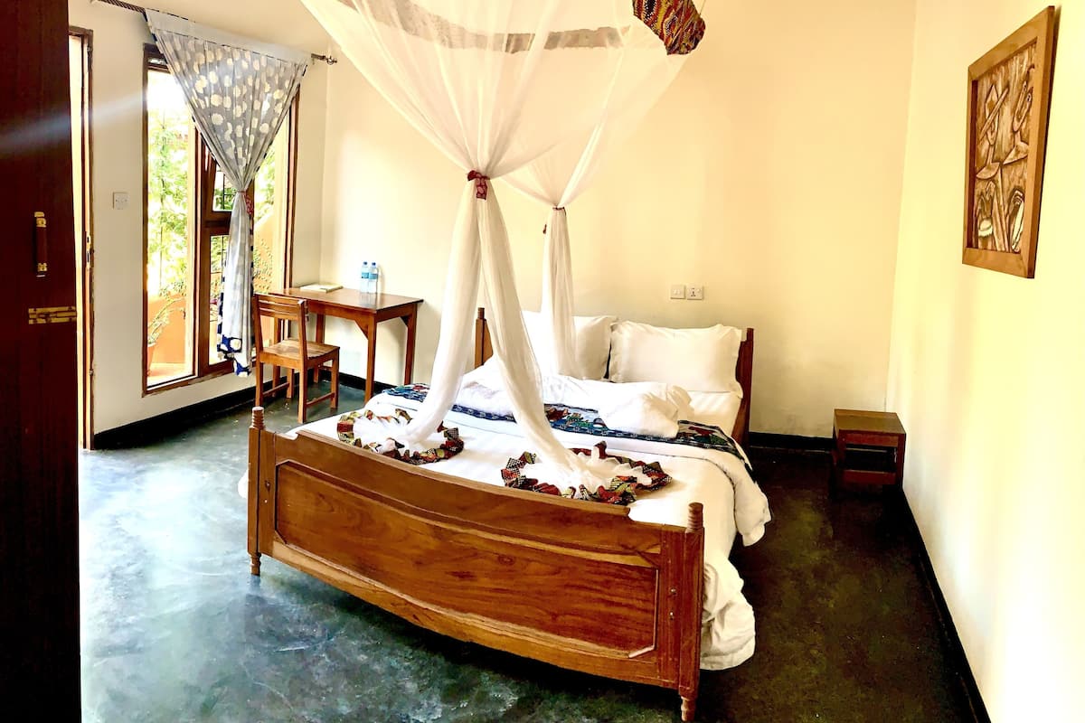 A room with a wooden bed, a small table, a chair, and a mosquito net over the bed.