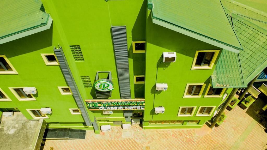 A green multi-story hotel with a rooftop terrace, multiple windows, and a visible logo.
