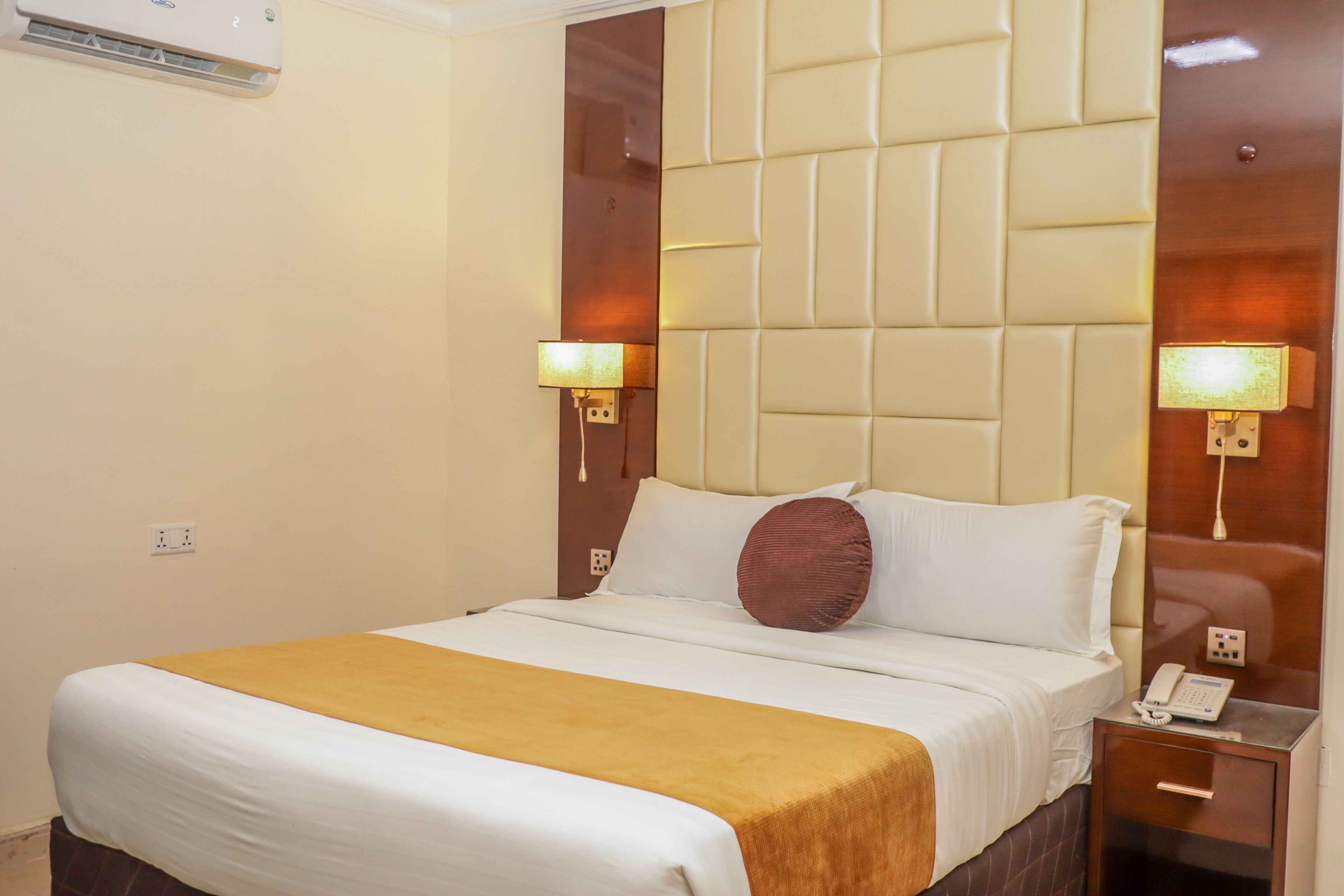 A hotel room with a large bed, a bedside table with a phone, and a wall-mounted light fixture.