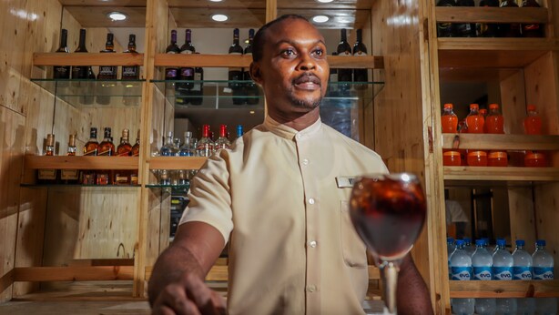 Un intérieur en bois avec des étagères remplies de bouteilles et une personne tenant un verre de vin.
