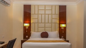 Une chambre d’hôtel avec un grand lit, deux lampes de chevet, un bureau avec une chaise et un climatiseur fixé au mur.