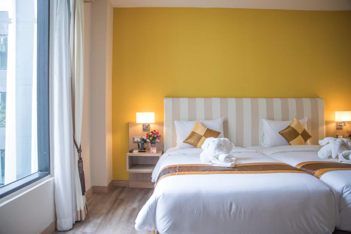 Quarto de hotel com duas camas, mesa de cabeceira e luminária, e janela com cortinas.