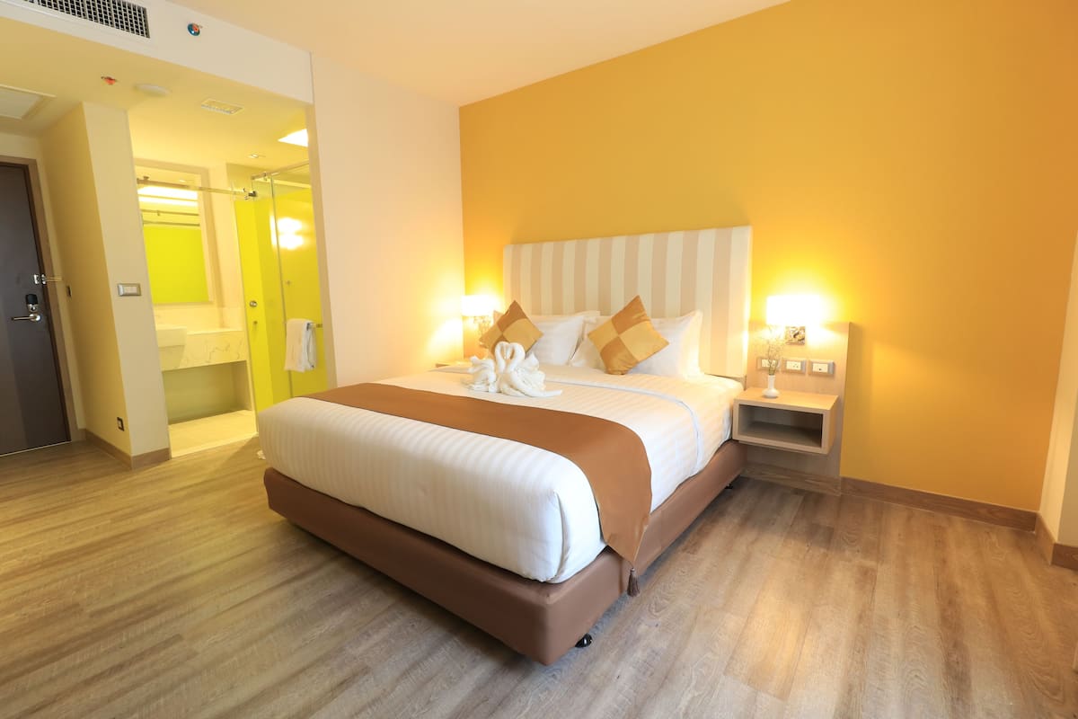 A hotel room with a large bed, bedside tables, a bathroom visible through an open door, and a yellow wall.