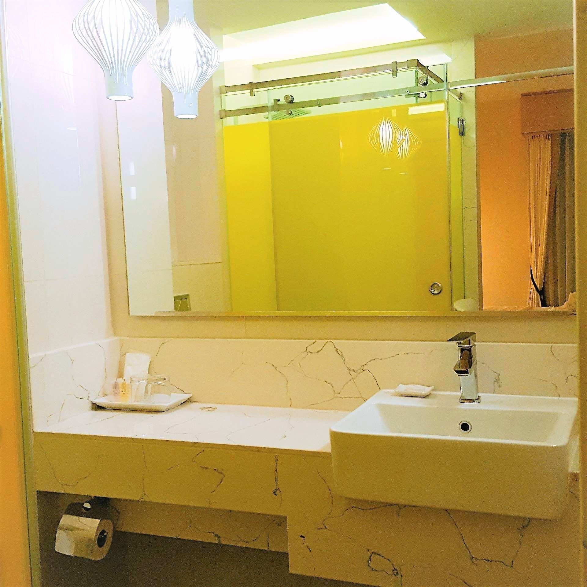 Ein Badezimmer mit einer weißen Marmorplatte, zwei Waschbecken, einem Spiegel und einer sichtbaren Dusche im Spiegelbild.