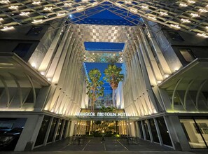 Hotel Bangkok Midtown, con un diseño arquitectónico moderno, que presenta una entrada destacada y una palmera en el centro.