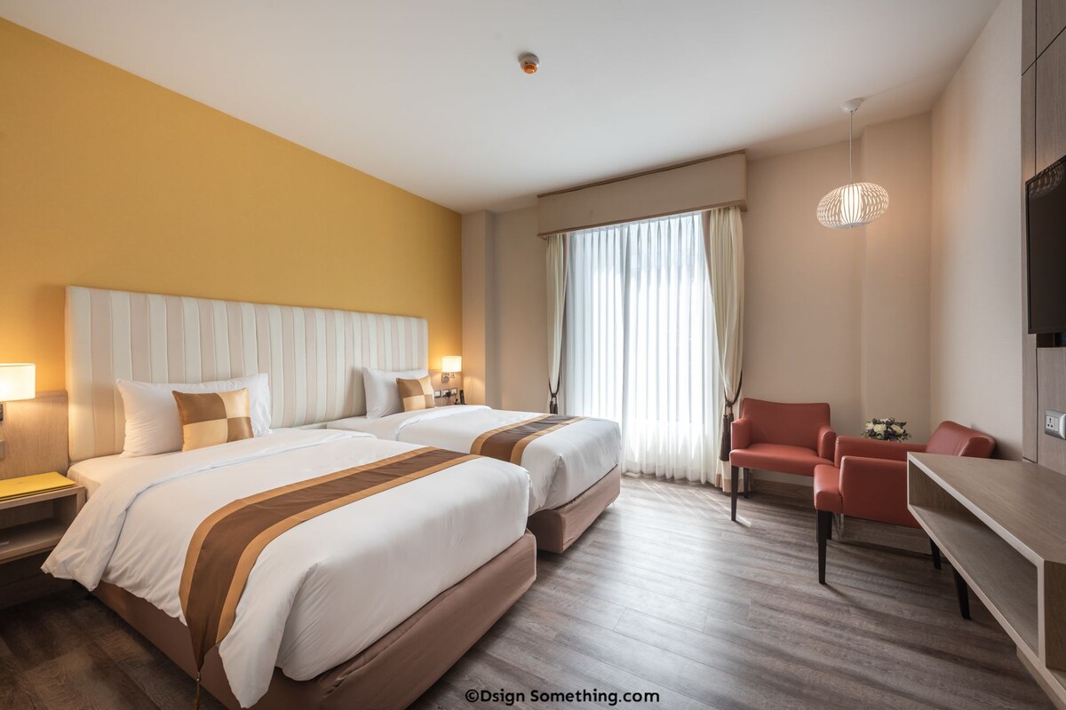 A hotel room with two beds, a desk, a chair, and a TV.
