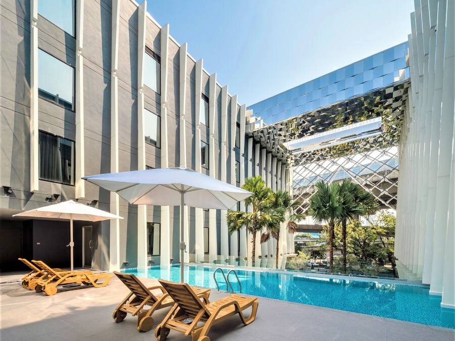 Un hotel moderno con piscina, tumbonas y palmeras.