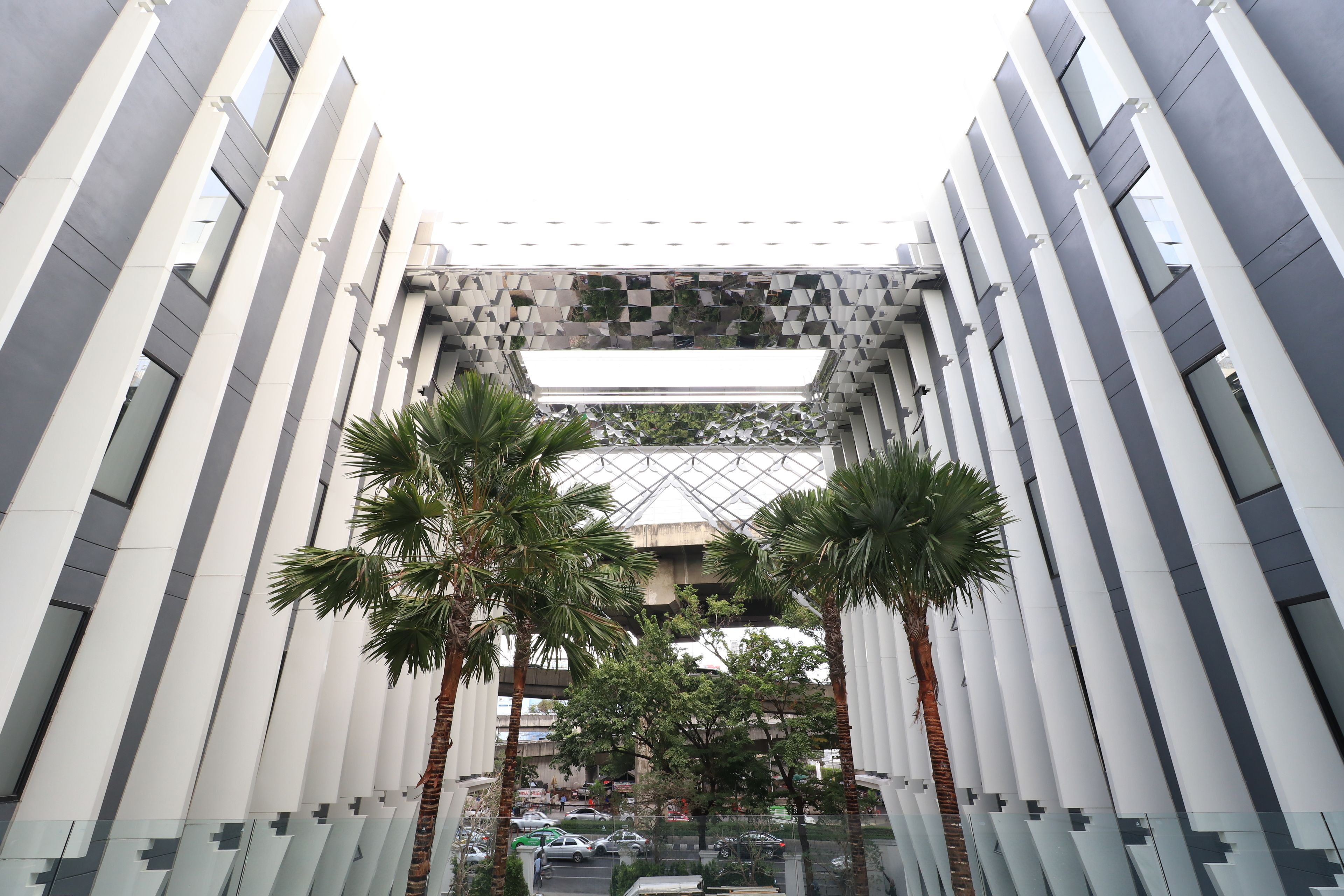 A modern building with a geometric facade, palm trees, and a glass ceiling.