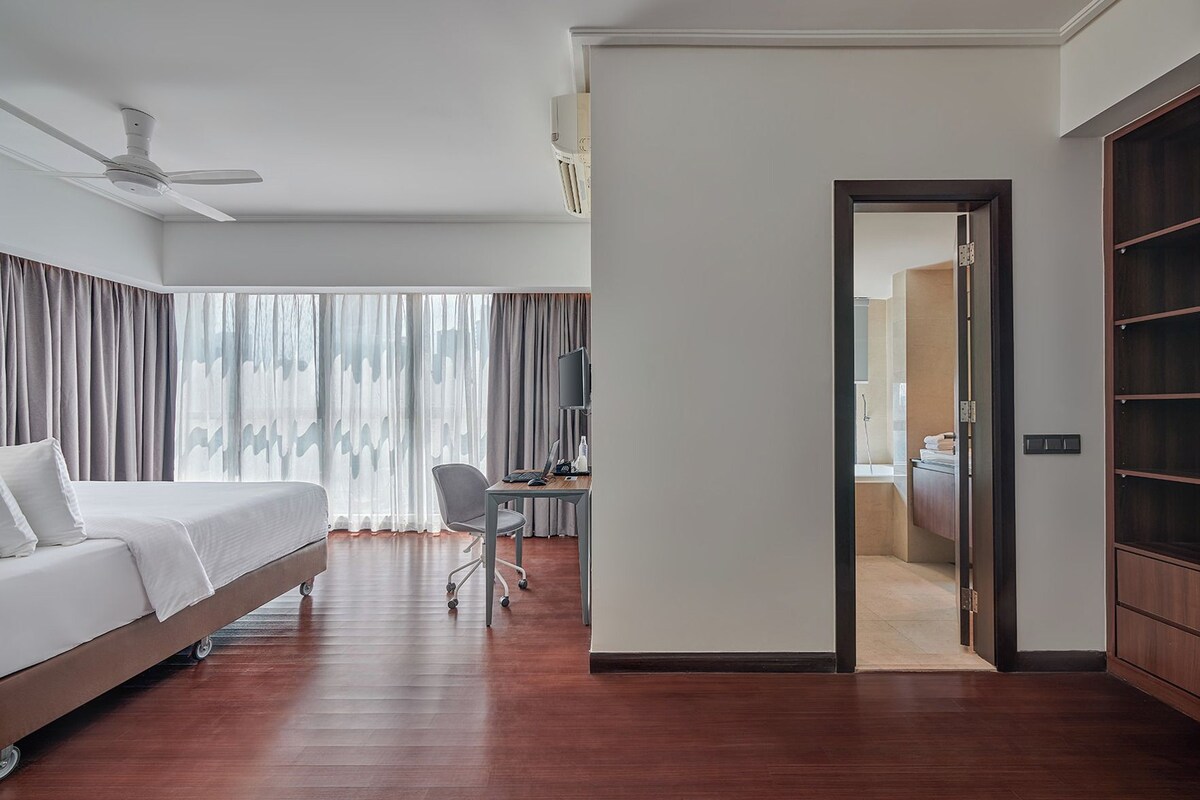 A hotel room with a bed, desk, chair, and a view through a door to a bathroom.