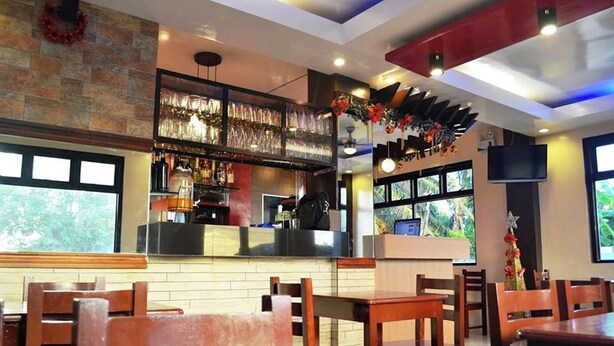 A restaurant interior with wooden tables and chairs, a bar area with a counter, and large windows providing natural light. - Casa Del Camba Hotel and Restaurant near Hundred Islands (Alaminos)