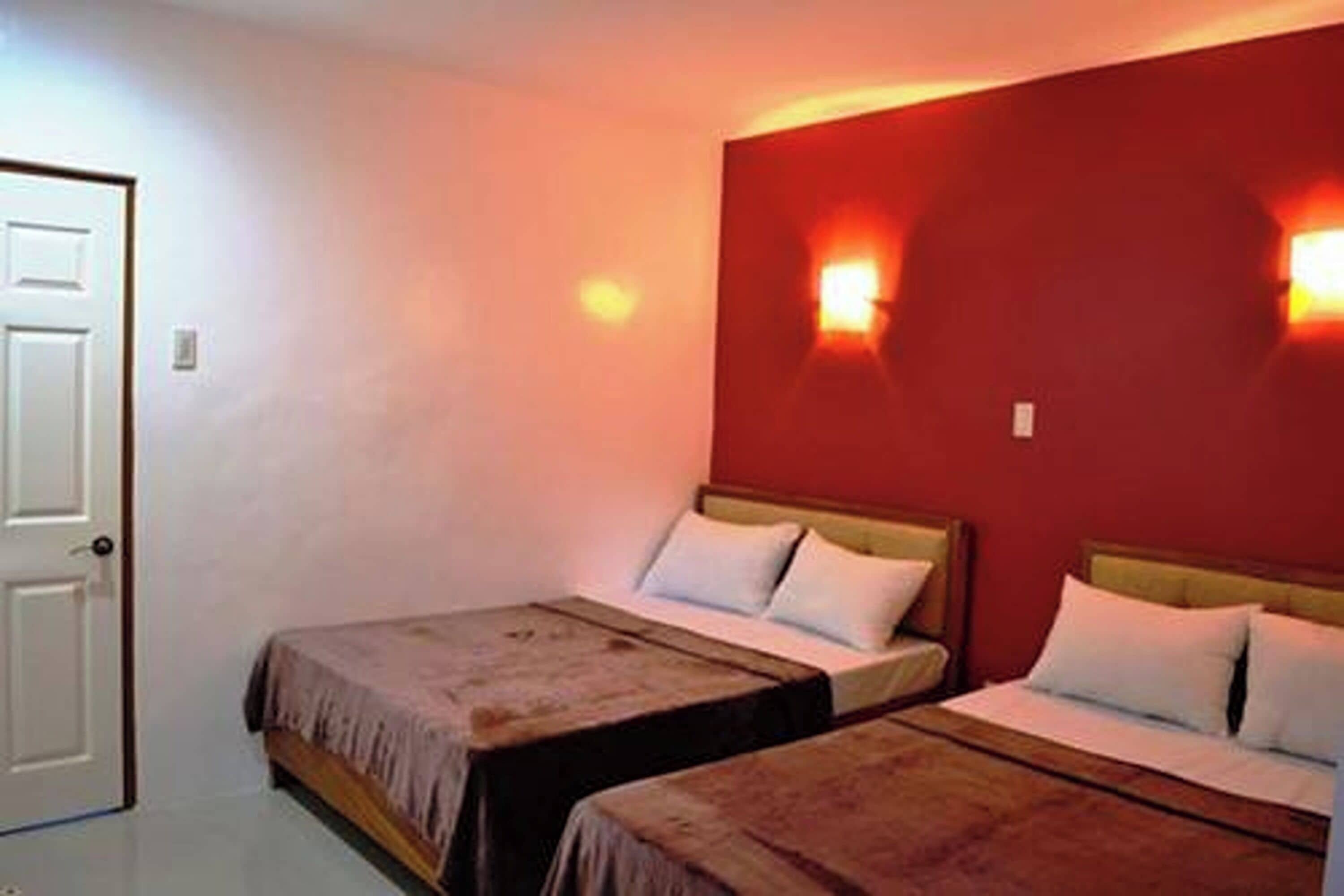 Una habitación con dos camas, una puerta y luces fijadas a la pared.