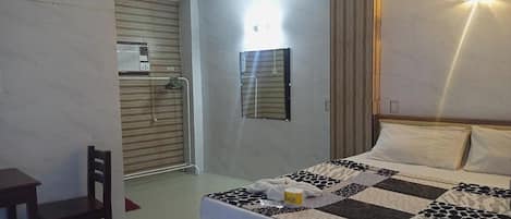 Habitación de hotel con cama, escritorio, silla, espejo en la pared y aire acondicionado.