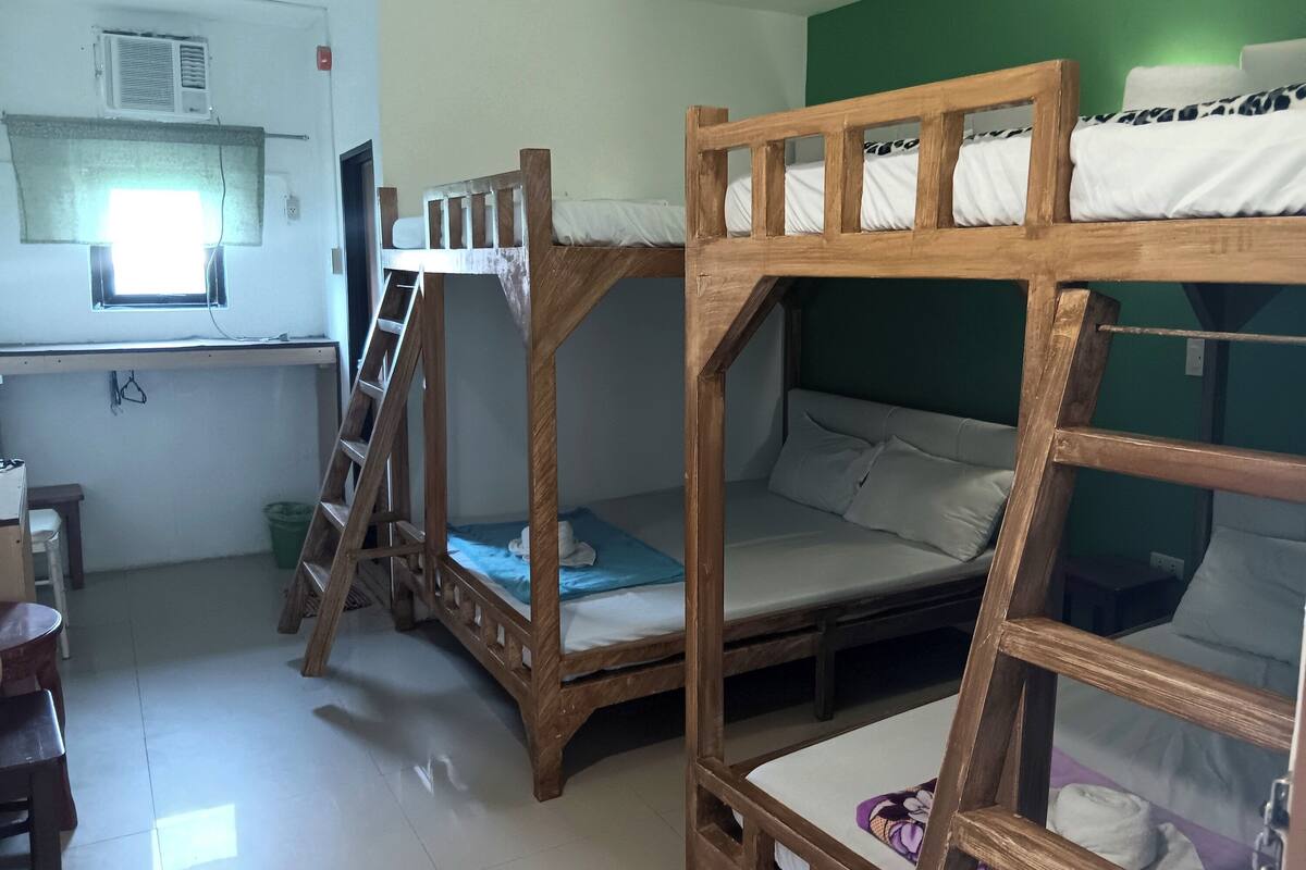 A bunk bed room with a desk, ladder, and a window with a curtain.