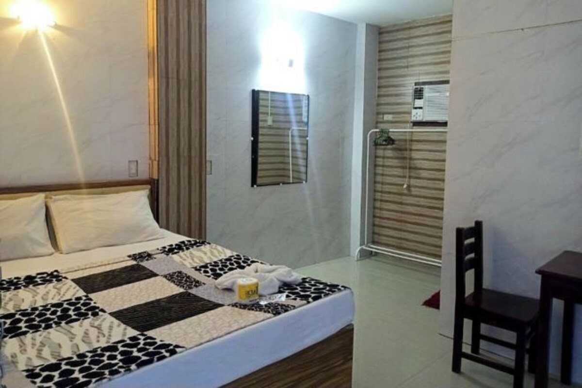 A hotel room with a bed, a chair, a desk, a shower, and a wall-mounted air conditioning unit.