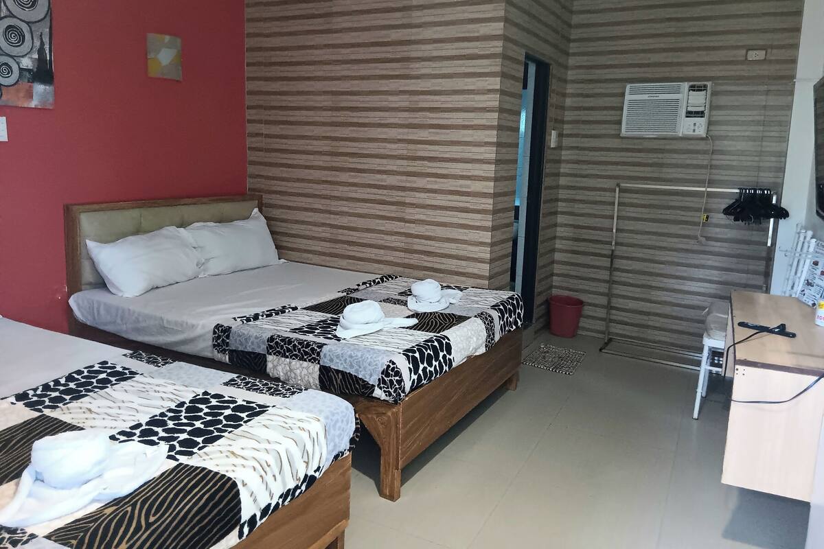 A hotel room with two beds, a desk, and an air conditioning unit.