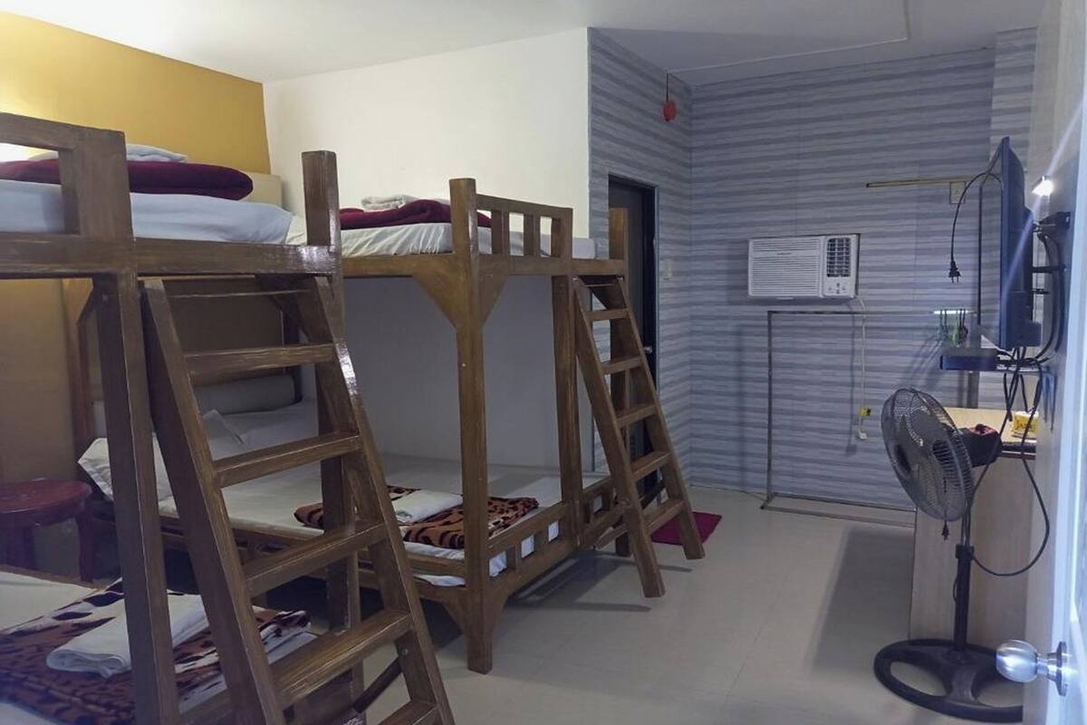 A room with bunk beds, a desk, a chair, a fan, and an air conditioning unit.
