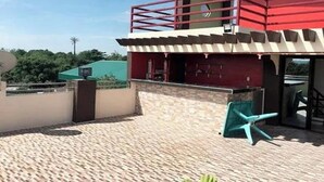 A building with a red and white exterior, a balcony, and a paved patio area with a chair. - Casa Del Camba Hotel and Restaurant near Hundred Islands (Alaminos)
