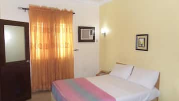 A bedroom with a bed, a door, a window with curtains, an air conditioning unit, and a wall-mounted picture.