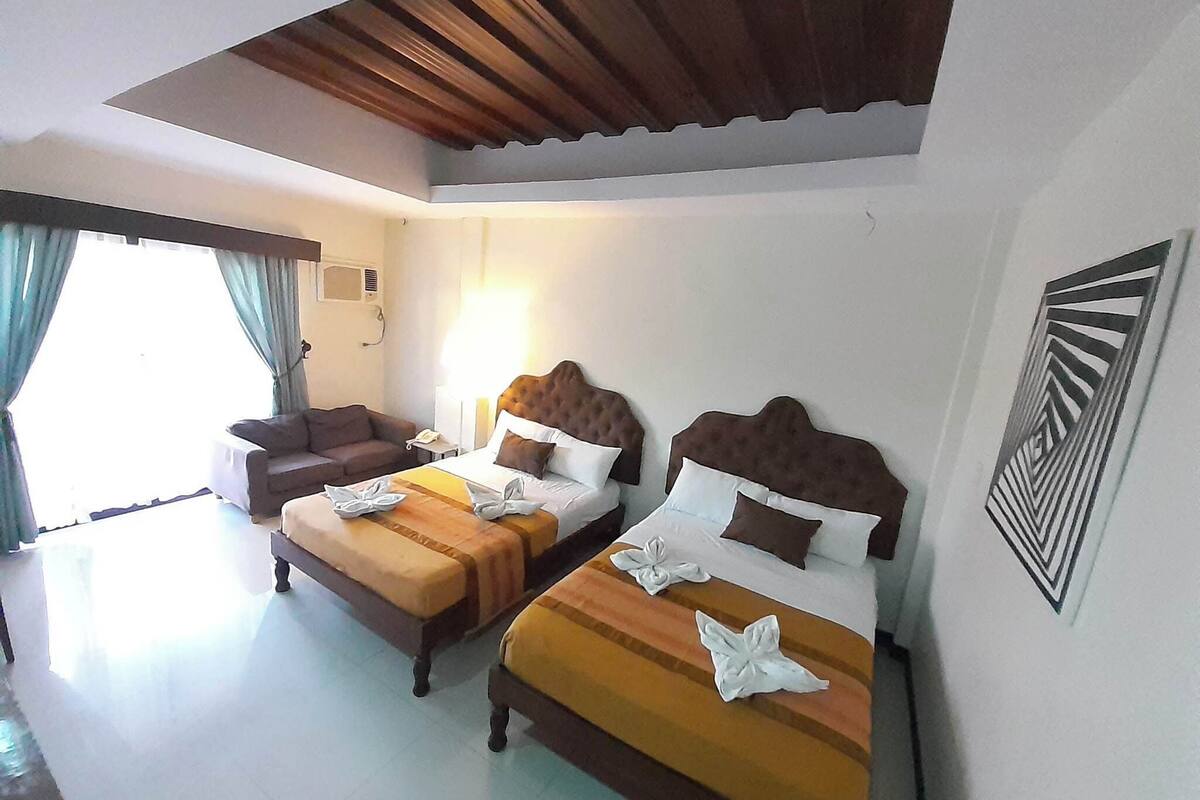 Habitación de hotel con dos camas, un sofá, una mesita de noche y una ventana con cortinas.