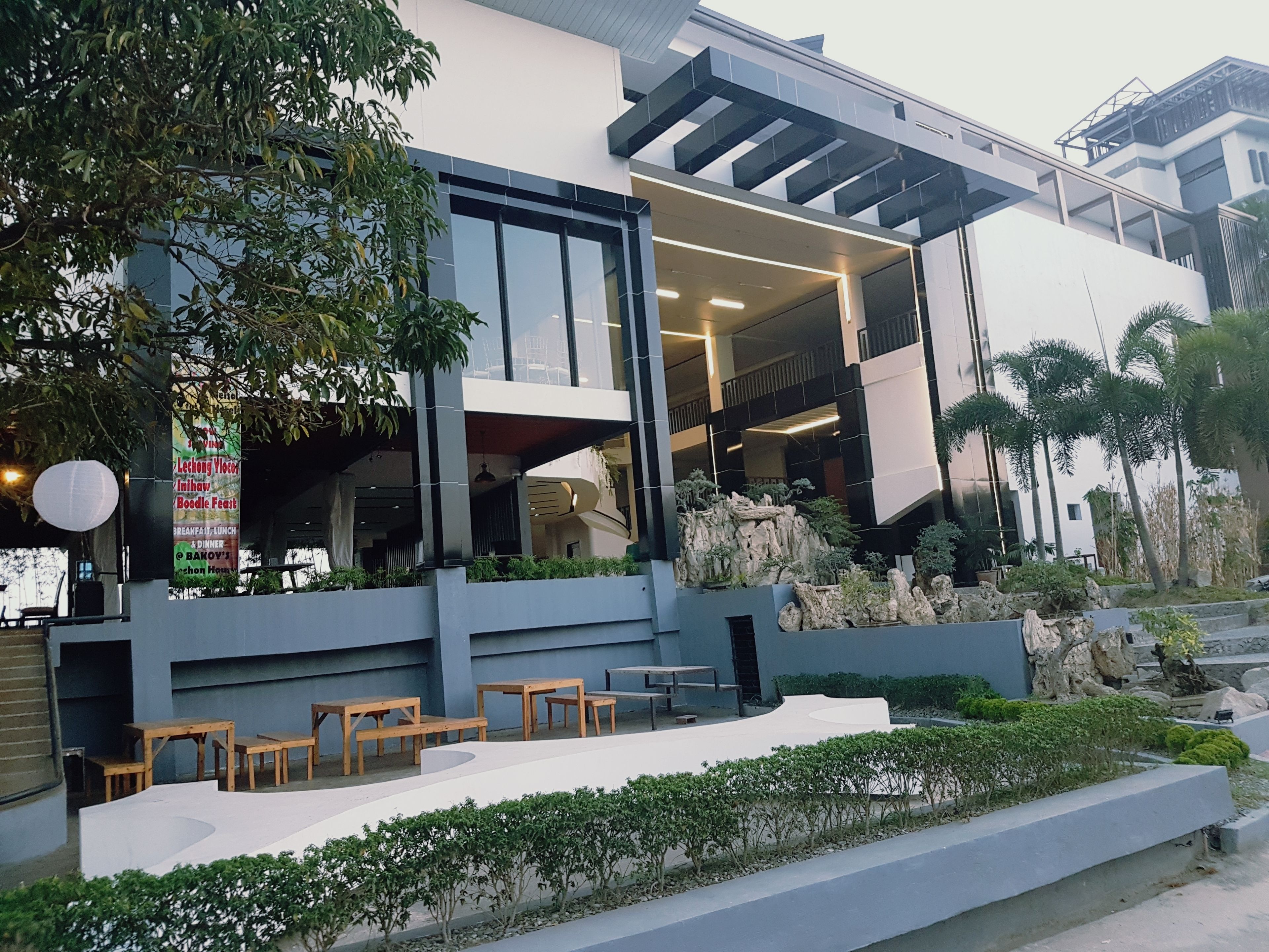 A modern building with a covered outdoor seating area, a rock garden, and a sign advertising a Boodle Feast.