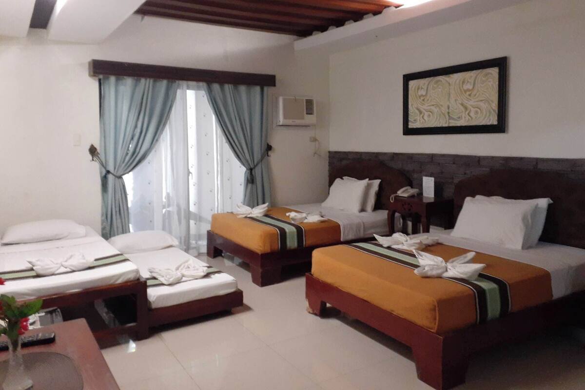 Habitación de hotel con dos camas, una mesita con un florero y un cuadro en la pared.