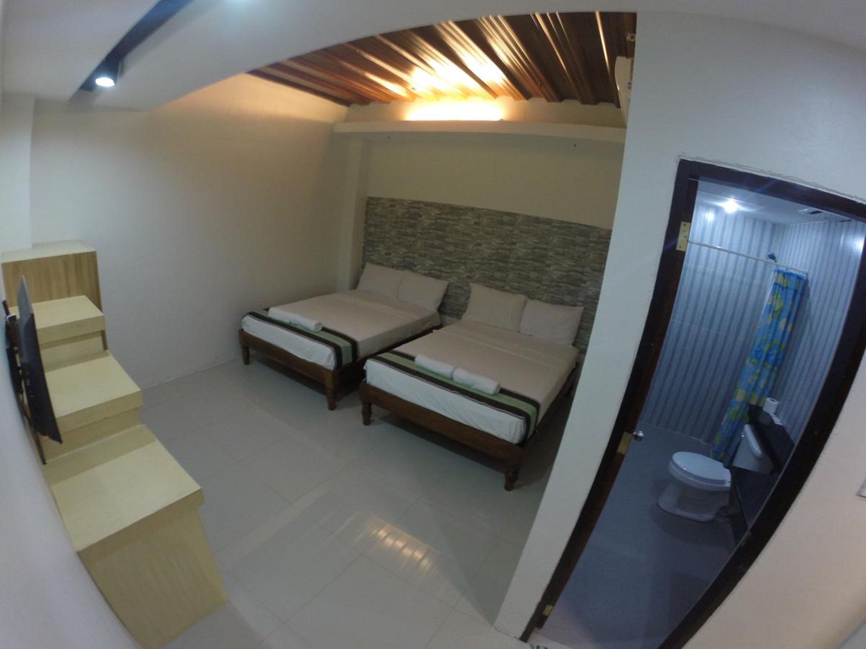Habitación compacta con dos camas individuales, baño pequeño con inodoro y ducha, y una escalera que lleva a un nivel superior.