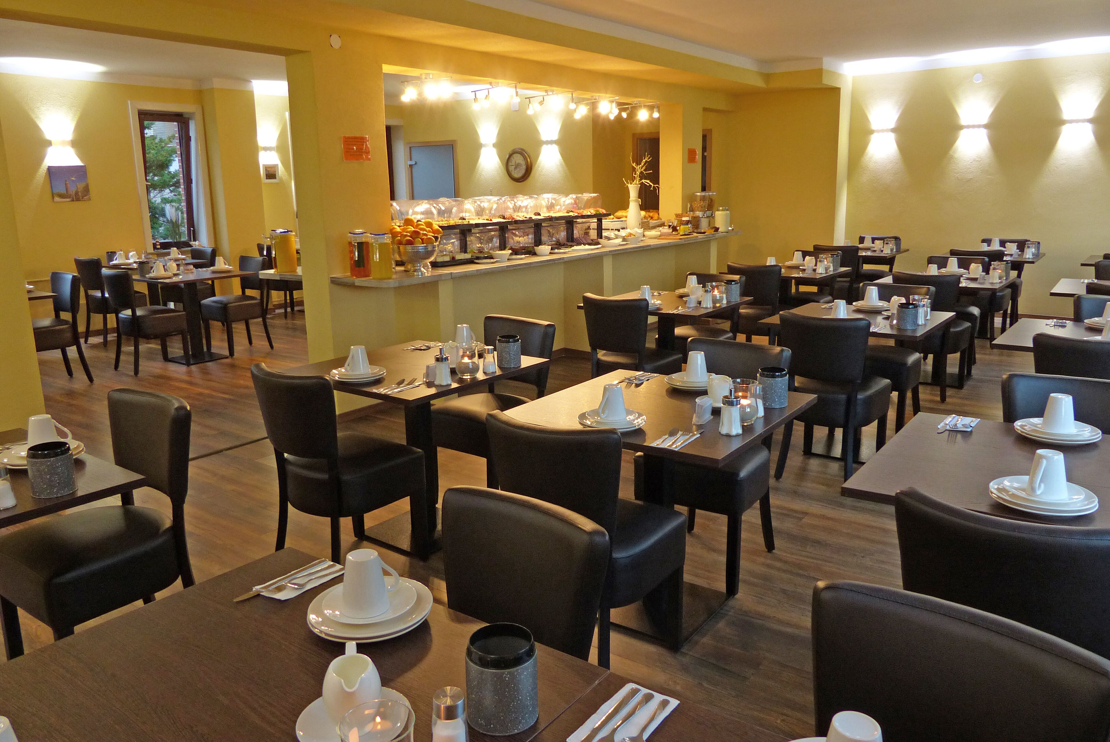 A restaurant with multiple tables and chairs, a buffet area with food and drinks, and a counter with a cash register.