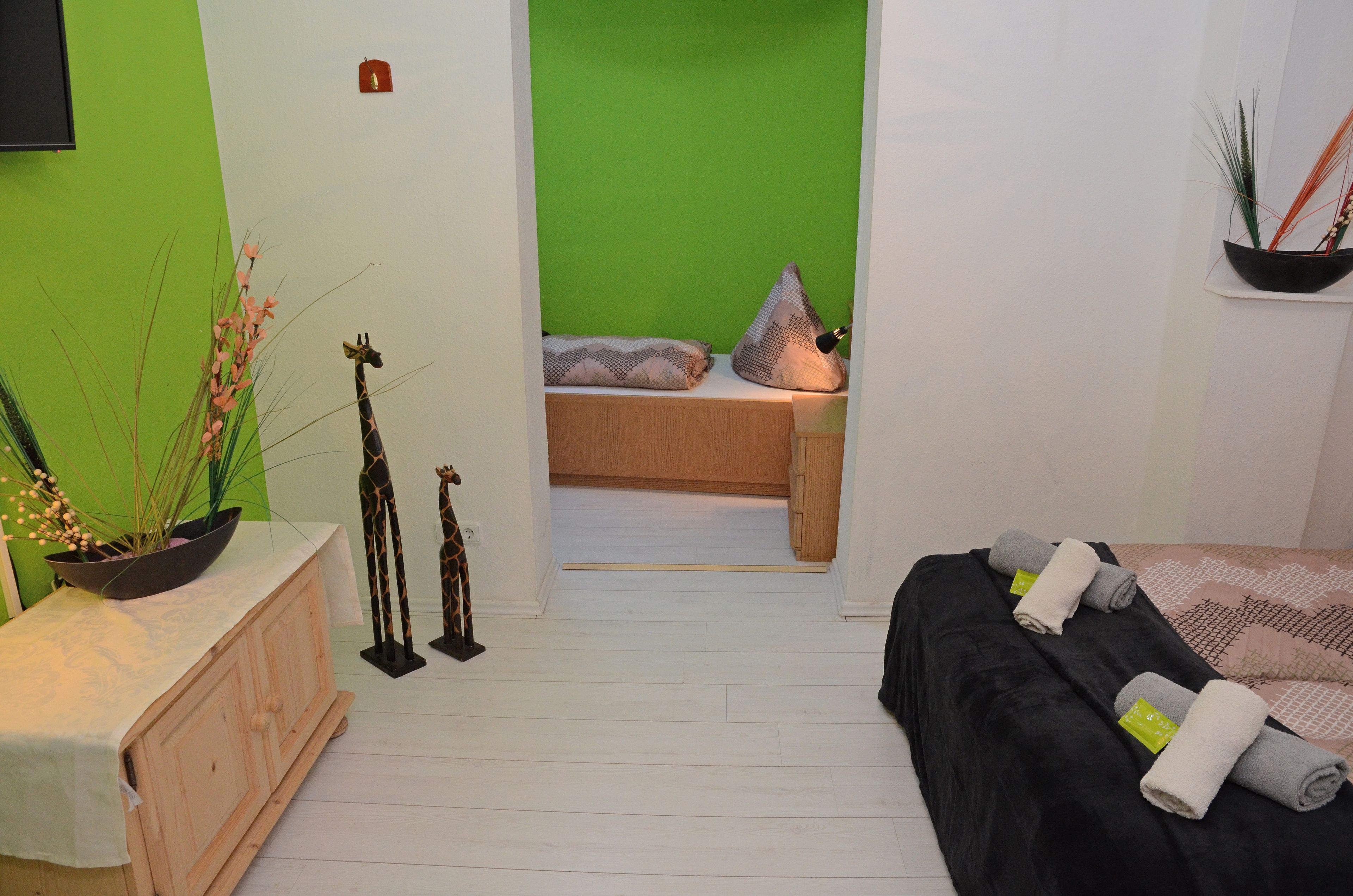 A room with a bed, a small table with a plant, and a green wall.