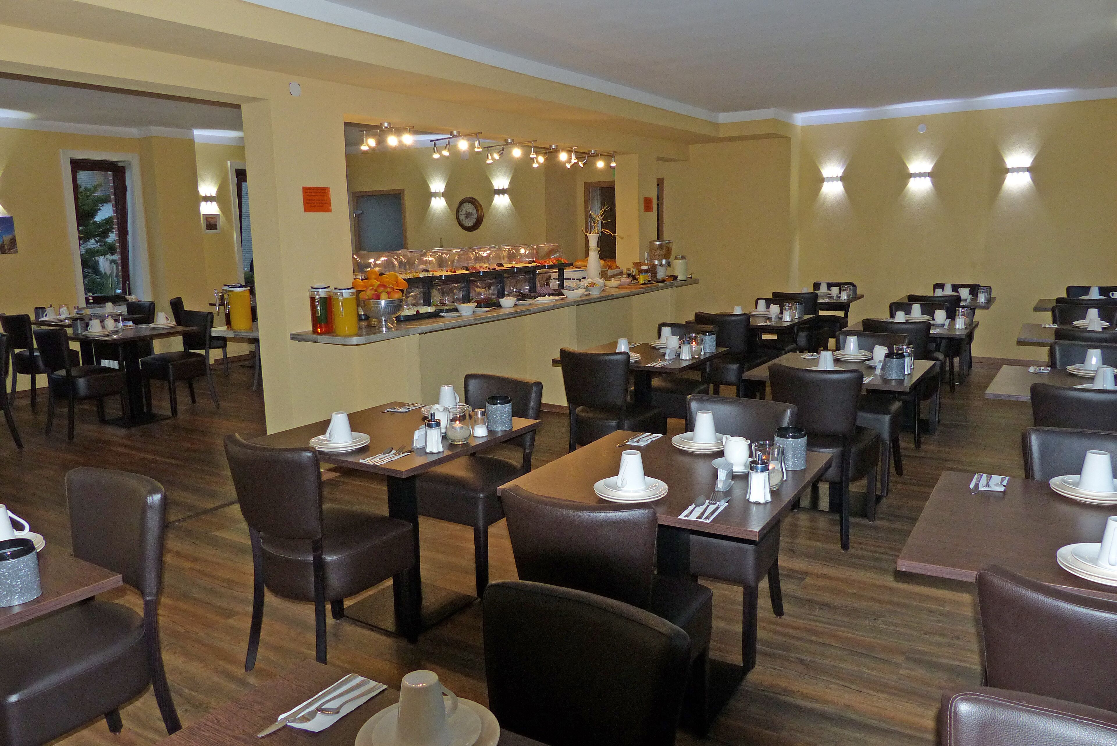 Un restaurant avec plusieurs tables et chaises, un buffet proposant divers plats, et une horloge au mur.