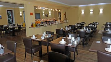 A restaurant with multiple tables and chairs, a buffet counter with various food items, and a clock on the wall.