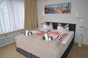 A neatly arranged bedroom with a bed, a window with curtains, a radiator, and a painting on the wall. - Neptuns Ankerplatz & Zur Seerobbe (Cuxhaven)