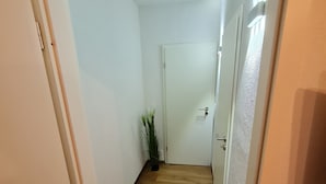 Un corridoio stretto con pavimento in legno e pareti bianche, che conduce a una porta chiusa.
