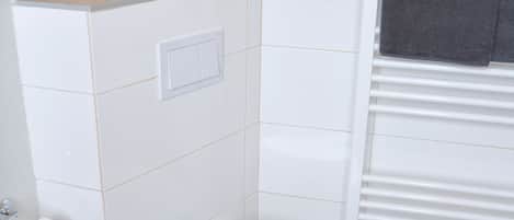 A bathroom with a white toilet, a small decorative lighthouse, and a towel rack with a towel.