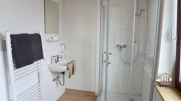 Un baño moderno con ducha de vidrio, un lavamanos con toalla y un espejo.