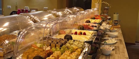 A buffet with various food items under clear covers, a clock on the wall, and a door in the background.