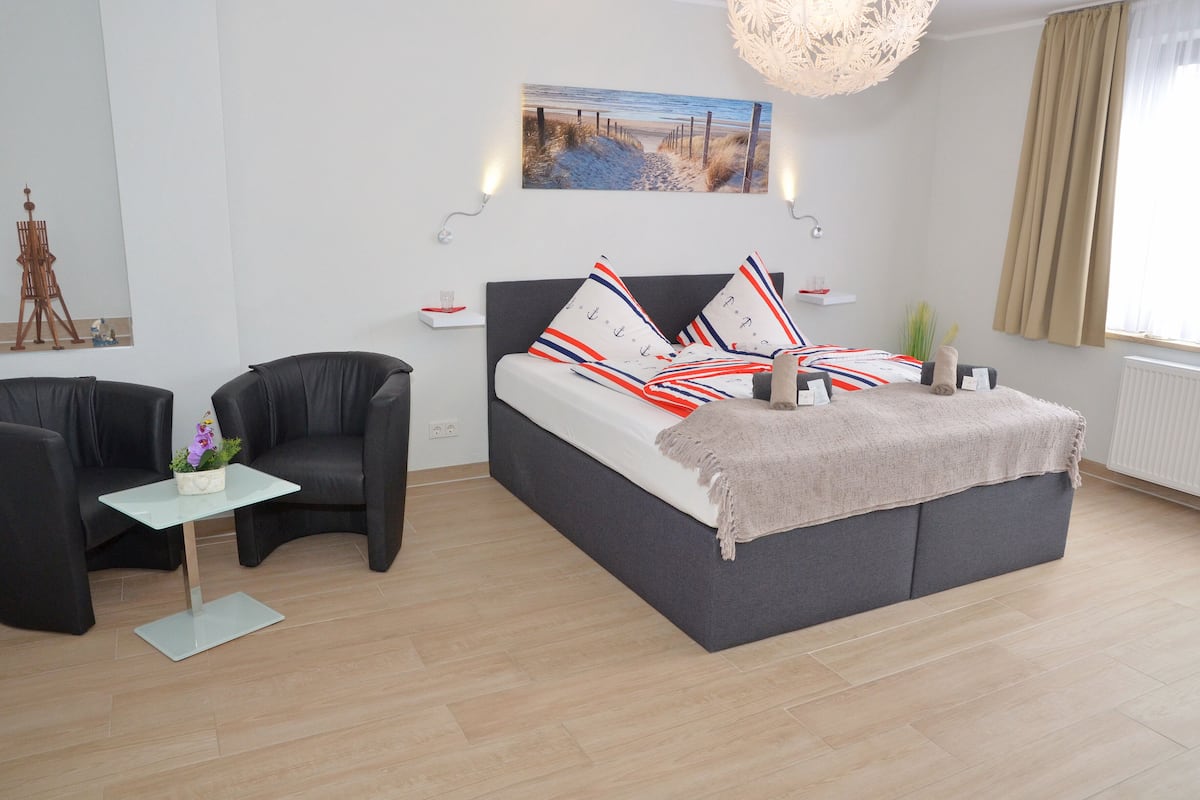 A modern bedroom with a bed, a small table, a chair, and a painting on the wall.