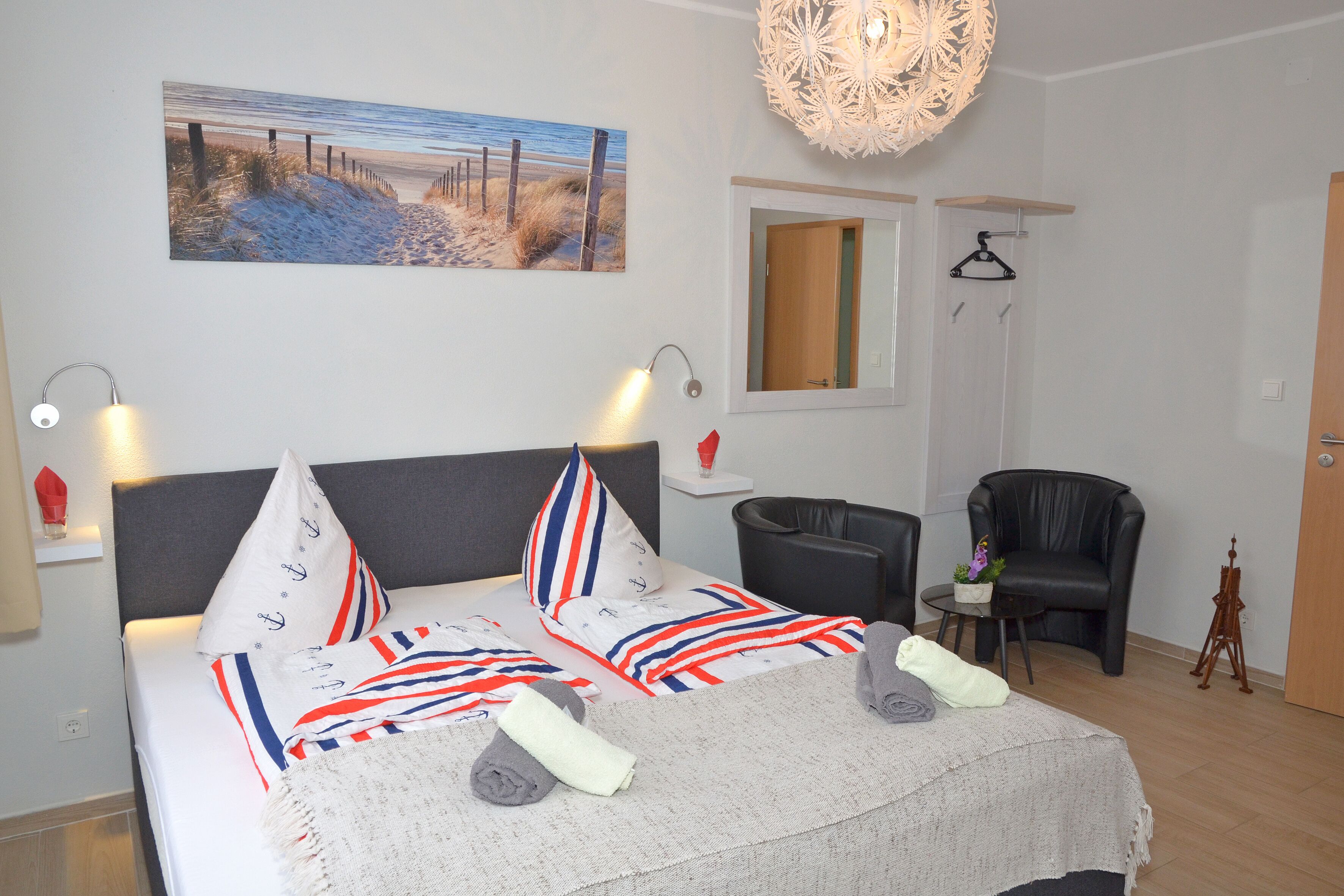 Ein ordentlich eingerichtetes Schlafzimmer mit einem Bett, Nachttischlampen, einem Sessel und einem Bild an der Wand.