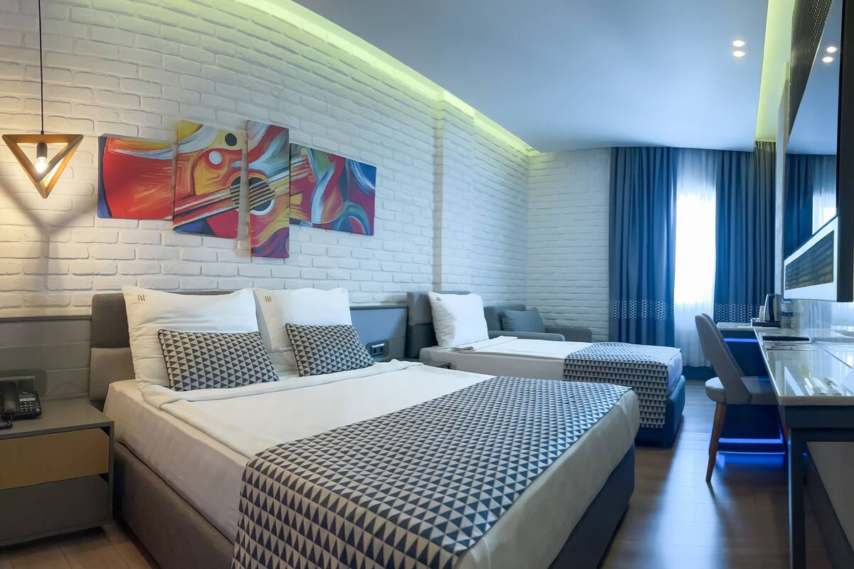 Une chambre d’hôtel moderne avec deux lits, un bureau et une grande fenêtre avec des rideaux.