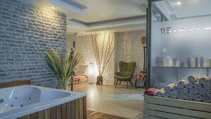 A spa room with a wooden bathtub, a green armchair, and a wall with a brick pattern.