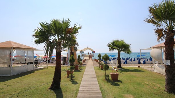 A beachside walkway leading to a beach area with palm trees, umbrellas, and beach chairs.
