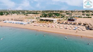 An aerial view of a beach with sun loungers, umbrellas, and a few people swimming in the water.